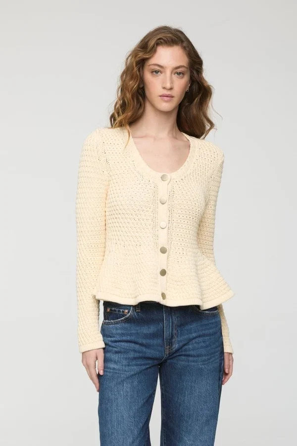 A woman modeling a cream-colored, textured knit cardigan sweater with button-front closure, paired with blue jeans, against a plain light gray studio background.