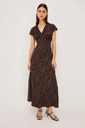 A woman modeling a dark brown midi wrap dress with a textured abstract pattern, short flutter sleeves, and a V-neckline, paired with black strappy sandals against a plain white studio background.