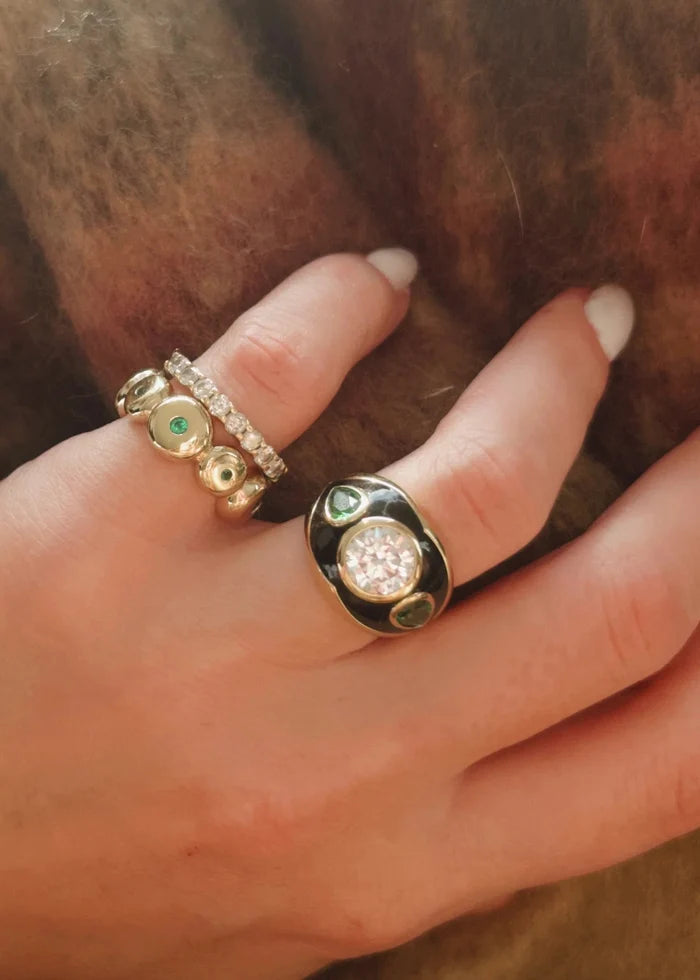 Hand wearing two gold rings with gemstones against a brown background