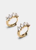 A pair of gold huggie hoop earrings with a curved top set with three clear marquise-cut gemstones, shown on a light gray background.