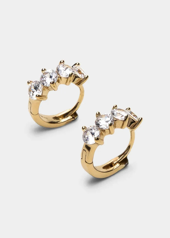 A pair of gold huggie hoop earrings with a curved top set with three clear marquise-cut gemstones, shown on a light gray background.