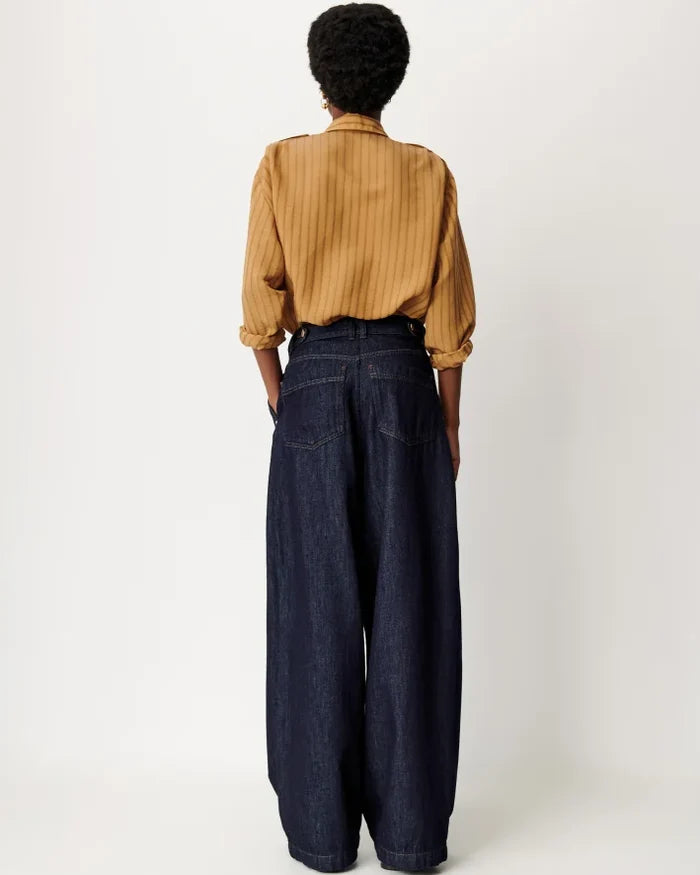 A person shown from the back wearing a mustard yellow vertically striped long-sleeve shirt and dark wide-leg denim jeans against a plain light gray studio background.