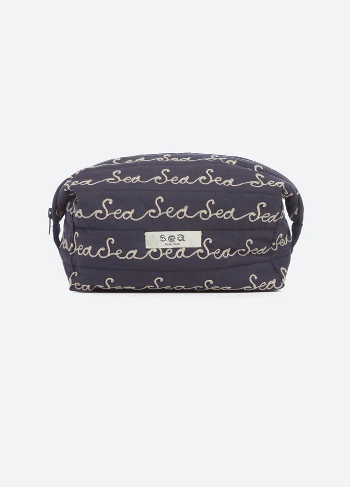 A navy blue quilted cosmetic pouch with an all-over beige script pattern reading 'Sea', featuring a small white brand label on the front.